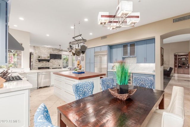 interior space featuring blue cabinets, exhaust hood, light tile patterned floors, appliances with stainless steel finishes, and backsplash