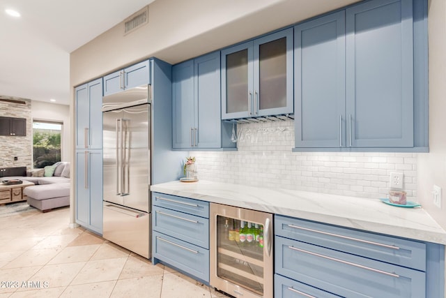 kitchen featuring backsplash, light stone countertops, blue cabinets, beverage cooler, and stainless steel built in fridge