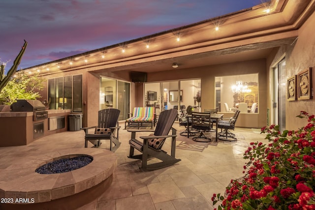 patio terrace at dusk featuring an outdoor kitchen, an outdoor fire pit, and grilling area