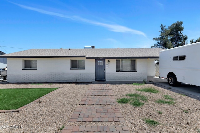 ranch-style home with roof with shingles and brick siding