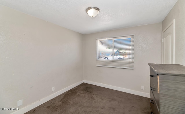 unfurnished room featuring dark carpet, a textured ceiling, and baseboards
