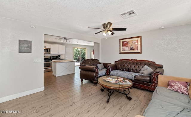 living room with visible vents, a textured ceiling, light wood finished floors, and a ceiling fan