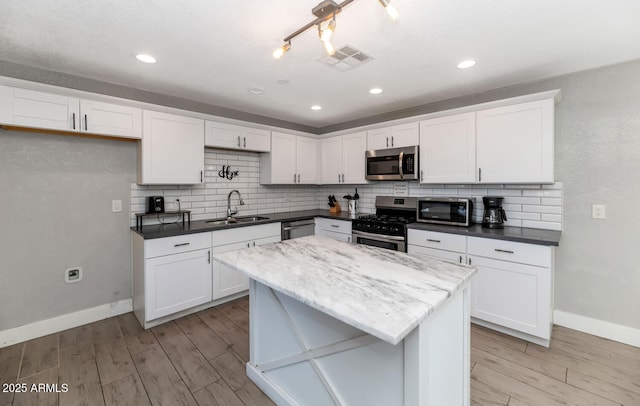 kitchen with appliances with stainless steel finishes, a sink, baseboards, light wood-type flooring, and visible vents