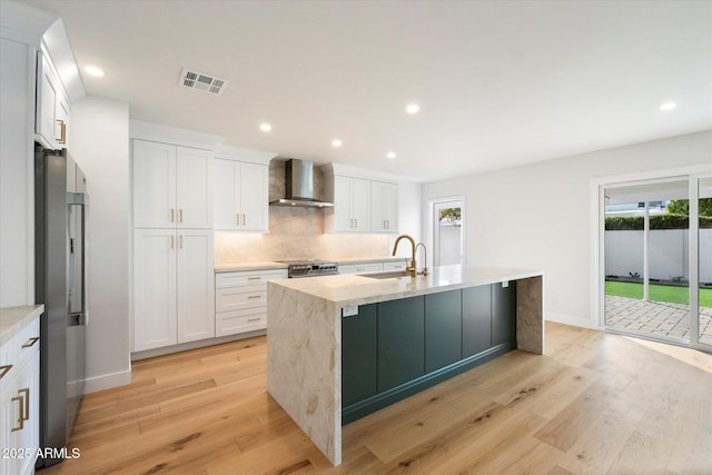 kitchen with sink, white cabinets, wall chimney range hood, a center island with sink, and light hardwood / wood-style flooring