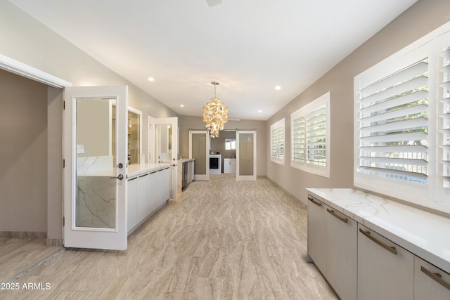 kitchen with a chandelier, light stone counters, white cabinets, and pendant lighting