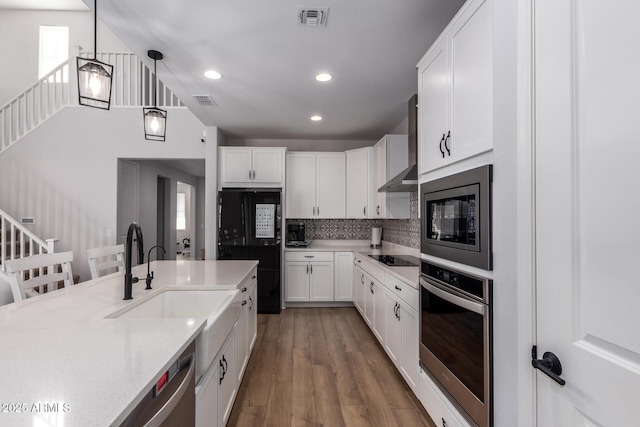 kitchen featuring wall chimney range hood, decorative light fixtures, black appliances, and white cabinets