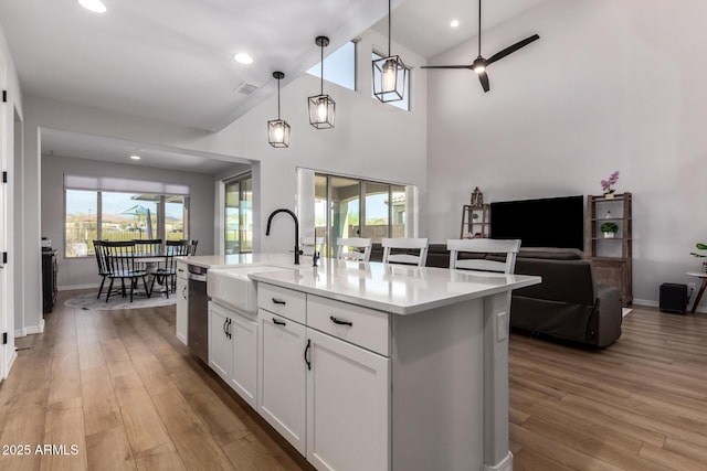 kitchen with sink, white cabinetry, decorative light fixtures, a center island with sink, and light wood-type flooring