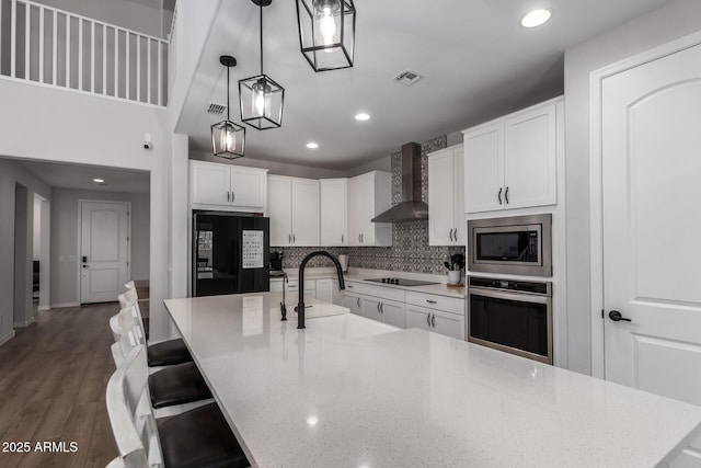 kitchen featuring pendant lighting, wall chimney range hood, sink, black appliances, and white cabinets