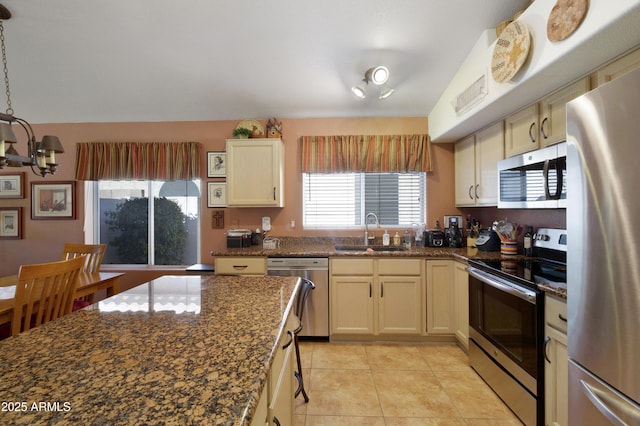 kitchen with a sink, dark stone countertops, appliances with stainless steel finishes, an inviting chandelier, and light tile patterned floors