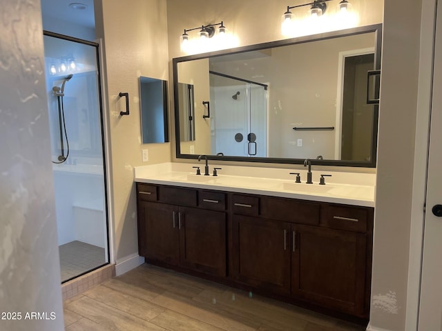 bathroom with a sink, wood finished floors, a stall shower, and double vanity