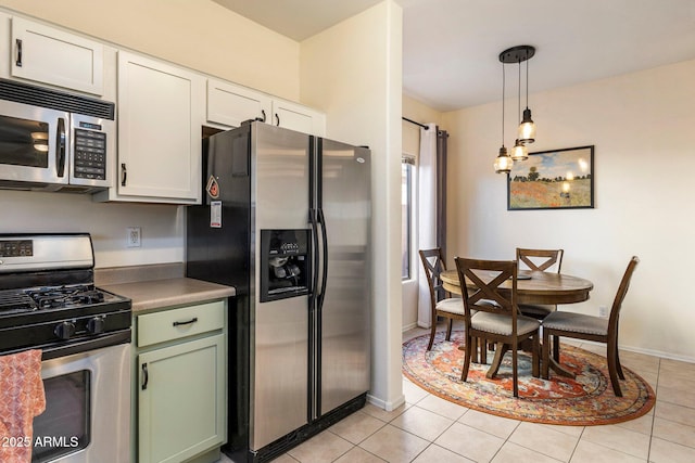 kitchen with light tile patterned floors, baseboards, white cabinets, appliances with stainless steel finishes, and hanging light fixtures