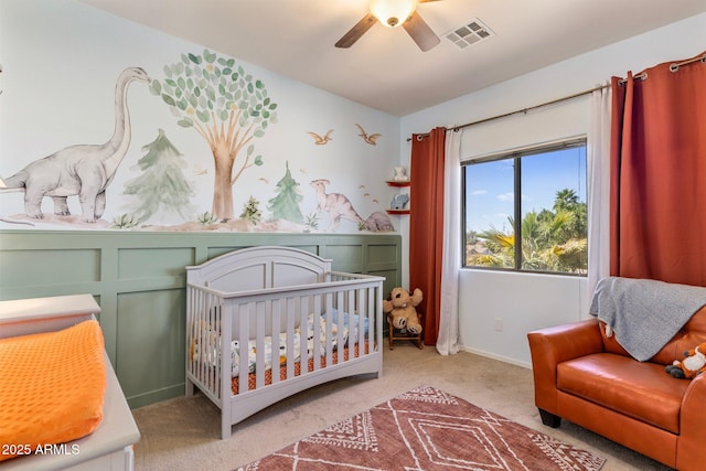 carpeted bedroom featuring ceiling fan, a crib, visible vents, and baseboards