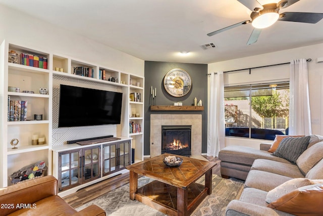 living area with built in features, a fireplace, visible vents, a ceiling fan, and wood finished floors