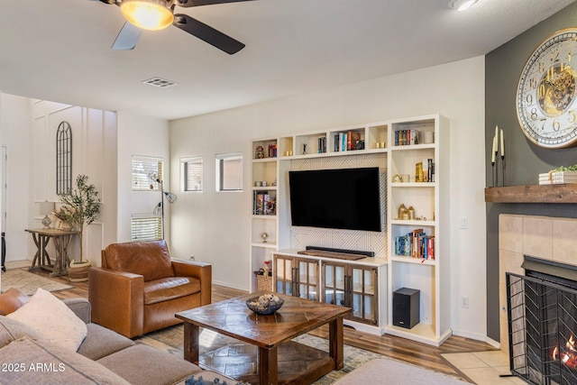 living room featuring visible vents, a tiled fireplace, a ceiling fan, wood finished floors, and baseboards