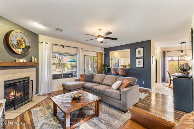 living room with visible vents, baseboards, a ceiling fan, light wood-style flooring, and a fireplace