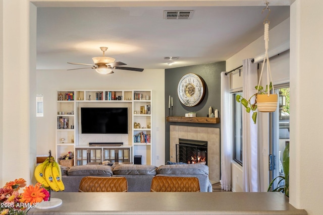 living area featuring a fireplace, visible vents, and a ceiling fan