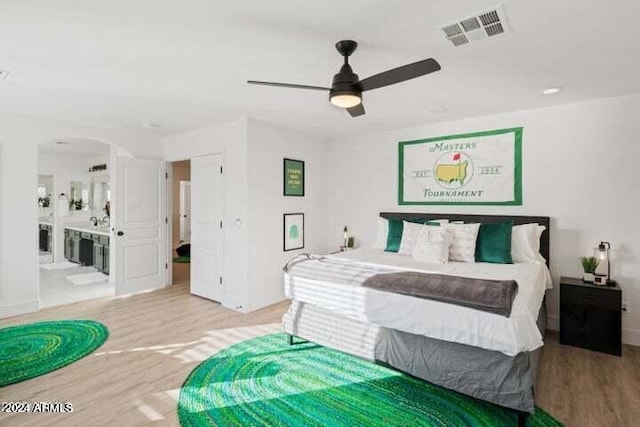 bedroom featuring visible vents, ensuite bathroom, wood finished floors, arched walkways, and ceiling fan