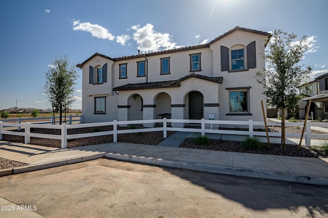 mediterranean / spanish house featuring stucco siding, a tiled roof, and a fenced front yard