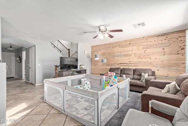 living room featuring ceiling fan, wooden walls, and light tile patterned floors