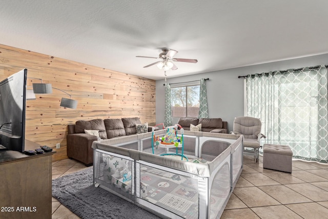 living room with ceiling fan, wooden walls, a textured ceiling, and light tile patterned floors