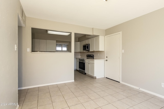 kitchen with appliances with stainless steel finishes, backsplash, light tile patterned floors, and white cabinetry