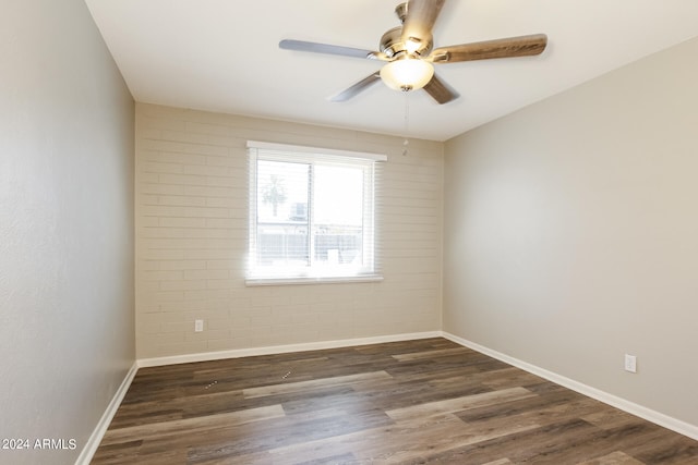 spare room featuring ceiling fan, dark hardwood / wood-style floors, and brick wall