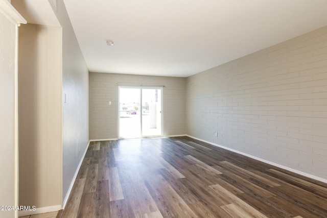 empty room with dark wood-type flooring and brick wall