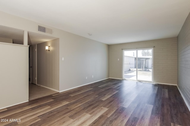 unfurnished room featuring brick wall and dark hardwood / wood-style flooring