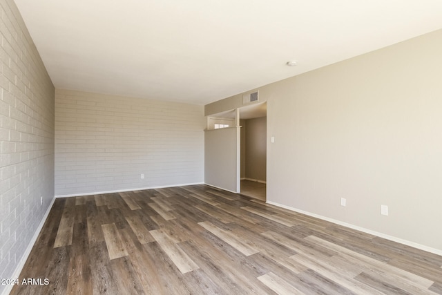 unfurnished room with brick wall and dark wood-type flooring