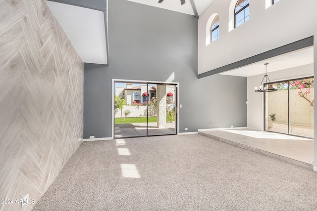 unfurnished living room featuring a high ceiling, a wealth of natural light, an inviting chandelier, and carpet flooring