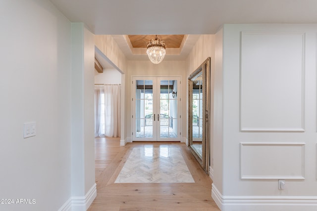 foyer entrance featuring a raised ceiling, french doors, a chandelier, and light wood-type flooring