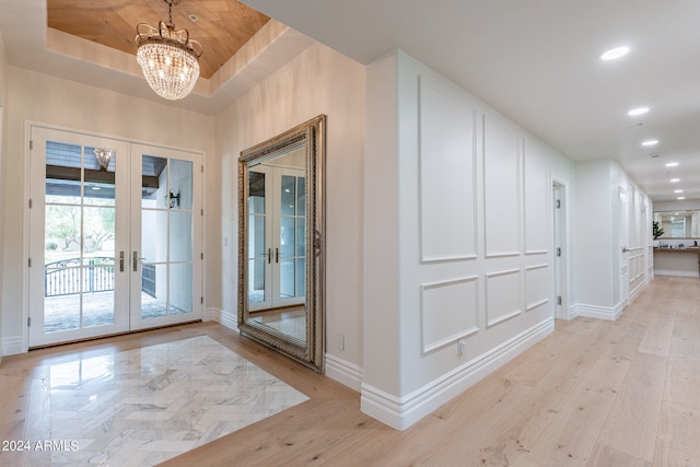 interior space featuring light wood-type flooring, french doors, a chandelier, and a raised ceiling