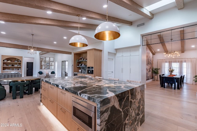 kitchen featuring hanging light fixtures, a spacious island, dark stone countertops, stainless steel microwave, and light hardwood / wood-style floors