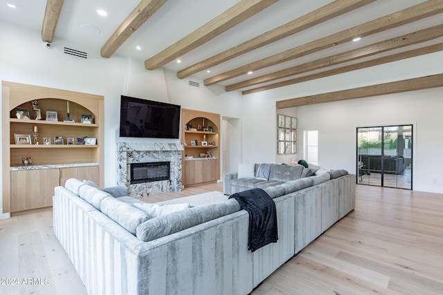 living room featuring light wood-type flooring, beamed ceiling, built in features, and a fireplace