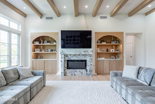 living room with light wood-type flooring, beam ceiling, and a stone fireplace