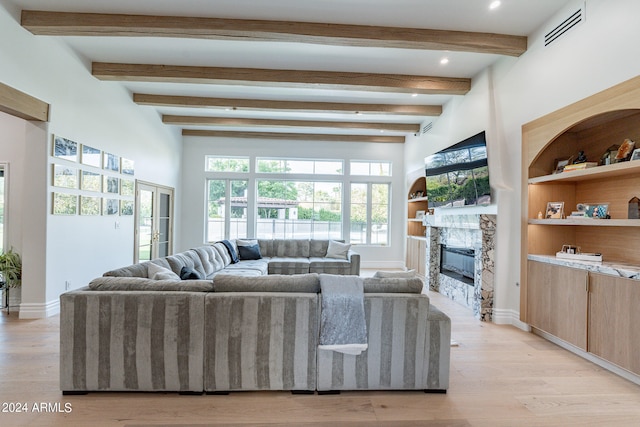 living room with a stone fireplace, beamed ceiling, and light hardwood / wood-style floors