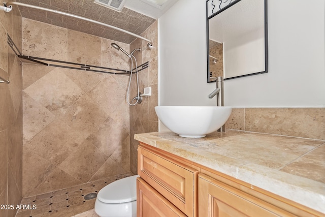 bathroom featuring a tile shower, vanity, and toilet