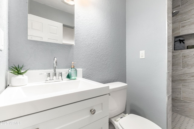 bathroom with tiled shower, vanity, and toilet