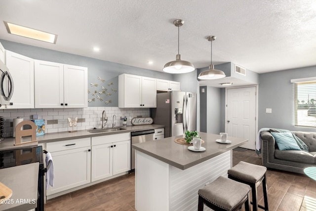 kitchen with a kitchen bar, sink, white cabinetry, hanging light fixtures, and stainless steel appliances