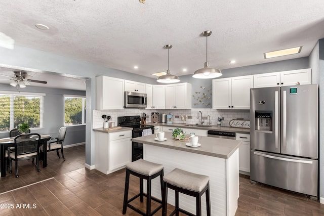 kitchen with a kitchen island, appliances with stainless steel finishes, white cabinets, and decorative light fixtures