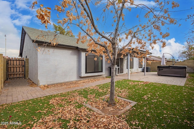 rear view of house with central AC unit, a lawn, a hot tub, and a patio