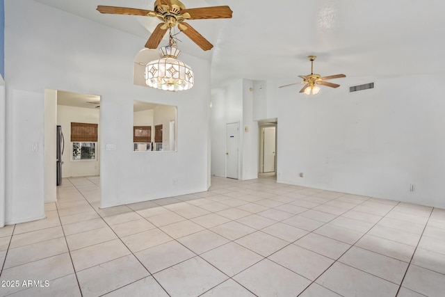 tiled empty room with high vaulted ceiling and ceiling fan with notable chandelier