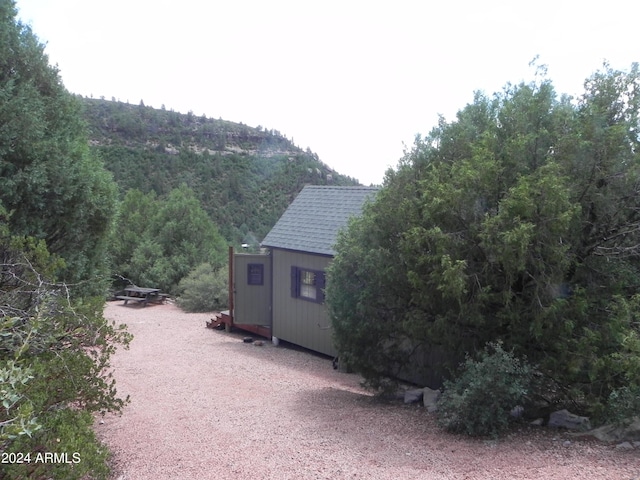 exterior space with a shingled roof, an outbuilding, and a storage unit