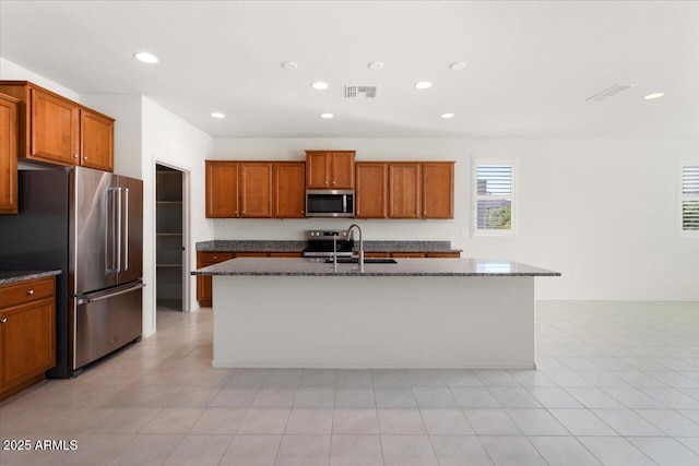 kitchen featuring stainless steel appliances, dark stone countertops, and a center island with sink