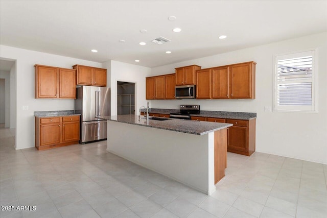 kitchen featuring sink, a center island with sink, dark stone counters, and appliances with stainless steel finishes