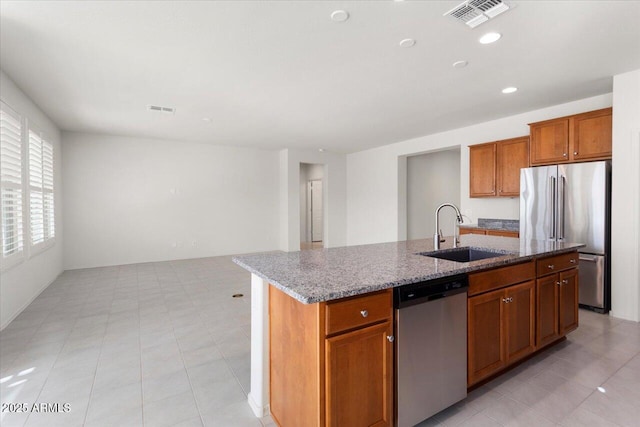 kitchen featuring sink, light stone countertops, an island with sink, and appliances with stainless steel finishes