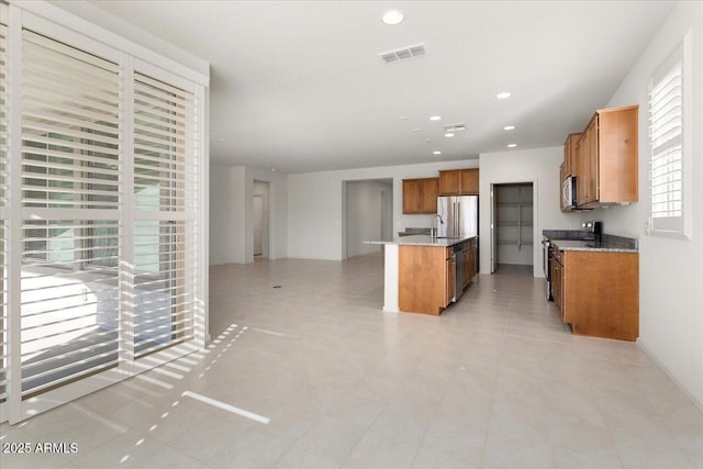 kitchen with sink, a center island, light stone counters, light tile patterned floors, and appliances with stainless steel finishes