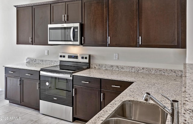 kitchen featuring light stone counters, light tile patterned floors, stainless steel appliances, dark brown cabinetry, and a sink