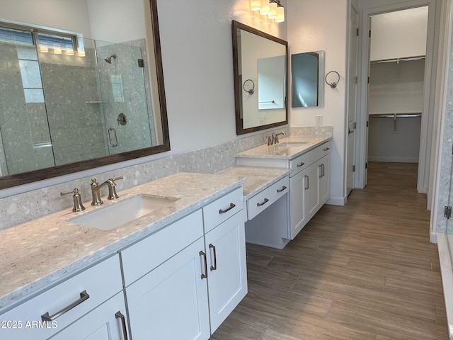 full bathroom with a shower stall, double vanity, a spacious closet, and wood finished floors