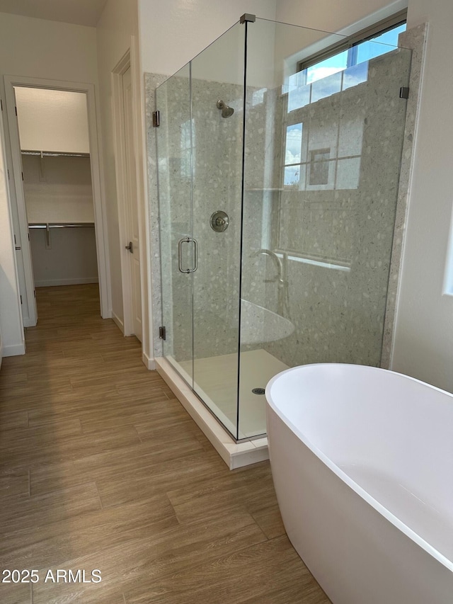 full bath with a stall shower, a soaking tub, wood finished floors, and a spacious closet